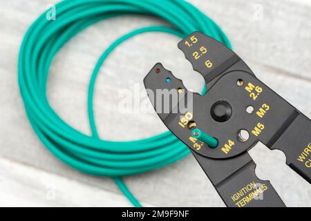 Close shot of Chinese made unbranded wire stripper & wire cutter for 26-10AWG wire (see Notes) with coiled role of green silicone covered wire. Stock Photo