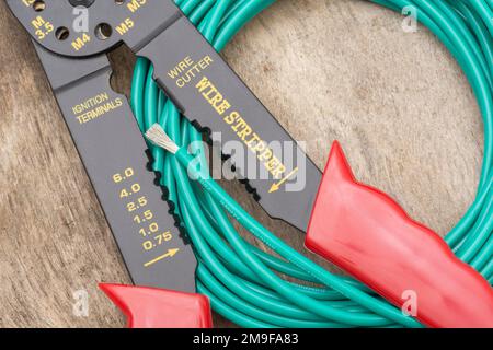 Close shot of Chinese made unbranded wire stripper & wire cutter for 26-10AWG wire (see Notes) with coiled role of green silicone covered wire. Stock Photo