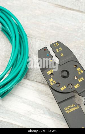 Close shot of Chinese made unbranded wire stripper & wire cutter for 26-10AWG wire (see Notes) with coiled role of green silicone covered wire. Stock Photo