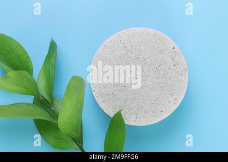 A podium made of concrete with green leaves, for the presentation of packaging and cosmetics, top view, on a blue background. Product display with whi Stock Photo