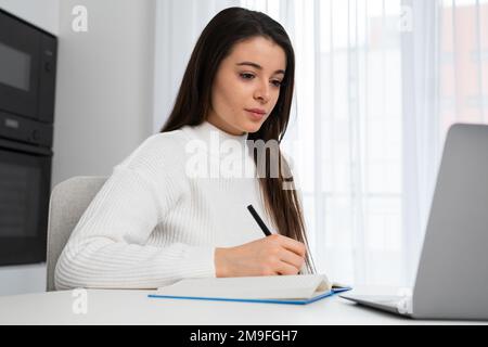 Modern female student in casual clothes studying remotely using laptop. Online education at home concept.  Stock Photo