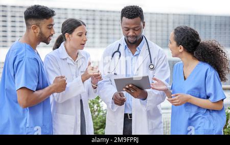 Solving problems as a team. a group of doctors using a digital tablet against a city background. Stock Photo