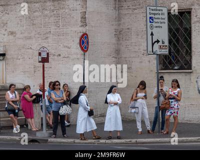 Two nuns are standing among a group of people at the public transport stop at the street in Rome Stock Photo