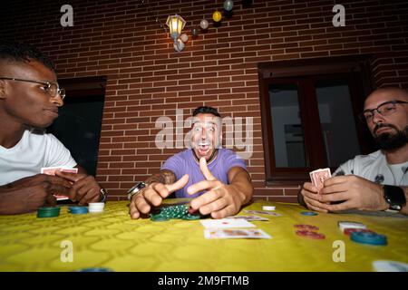 Happy and excited man wins in poker card game while playing with friends. Stock Photo