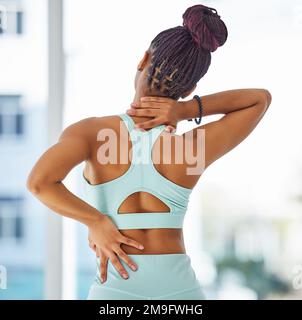 My back pain is affecting my neck now. an unrecognisable woman standing alone in a yoga studio and suffering from back and neck pain. Stock Photo