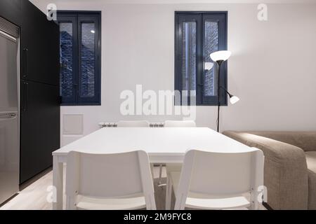 Dining room with white wooden table with matching chairs and blue wooden windows overlooking an interior brick patio Stock Photo