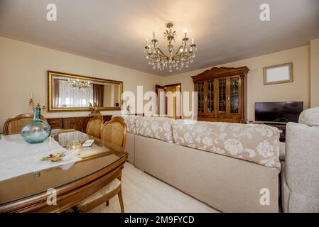 Dining room furnished with vintage-style wooden furniture with a mirror framed in golden wood and a chandelier with crystals Stock Photo