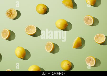 From above of fresh ripe halved and whole yellow lemons arranged on green surface as abstract background Stock Photo