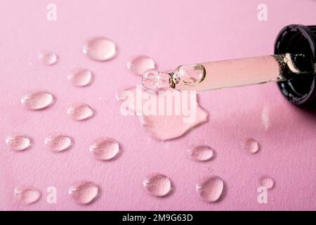 Close up view of glass dropper with oil and oil drops on pink studio background. Vitamin, essential oil or food supplement concept. Stock Photo