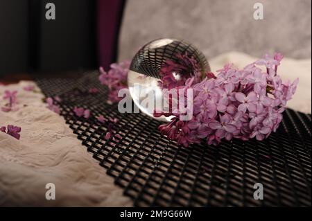 Glass lens ball and lilac flowers on metal grid. Horizontal photo with copy space. Stock Photo