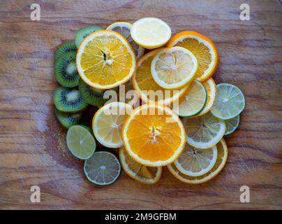 Sliced Orange, Lemon and Kiwi fruit piled up on a wooden chopping board Stock Photo