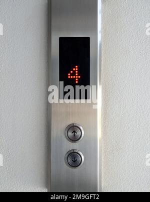 The arrow symbol with the braille on the push button of the metal panel in the passenger elevator, office building in the urban area, front view with Stock Photo