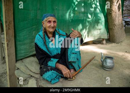 An old Kalash woman with traditional wear sitting on the ground, Bumburet Valley, Pakistan Stock Photo