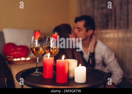 Valentines Day couple kissing at home. Close up of festive drinks wine with strawberries by burning red candles. Stock Photo