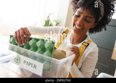 Close-up of smiling biracial young woman sorting paper garbage in recycling bin, copy space Stock Photo