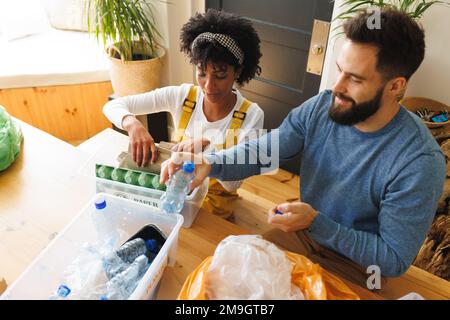High angle view of biracial young couple sorting papers and plastics garbage in bins on table Stock Photo