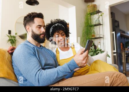 Biracial young couple using smartphone while relaxing on sofa in living room Stock Photo