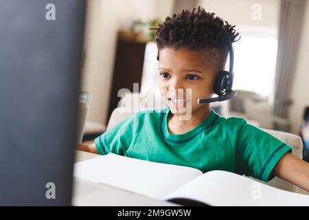 Happy african american boy sitting at table, using laptop for online lesson Stock Photo
