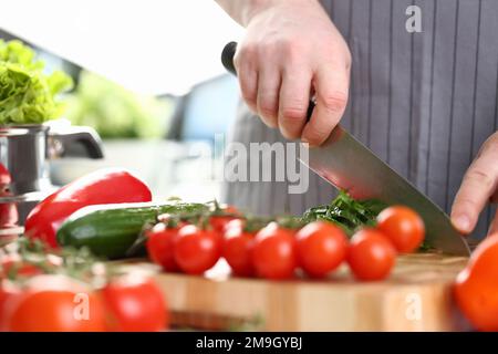 Cook cuts tomatoes and cucumbers on cutting board Stock Photo