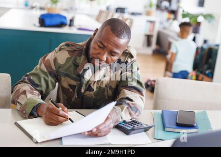 Happy african american man wearing military uniform sitting at table and working Stock Photo