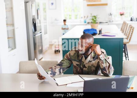 Happy african american man wearing military uniform sitting at table and working Stock Photo