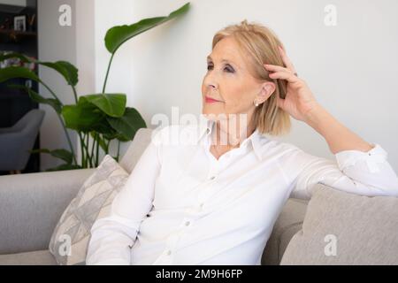 Portrait of beautiful senior woman with blonde hair sitting on the sofa at home. Stock Photo