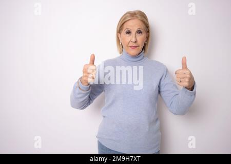 Senior woman over white background doing happy thumbs up gesture with hand. Approving expression looking at the camera showing success. Stock Photo