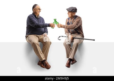 Cheerful elderly men sitting on a blank panel with bottles of beer isolated on white background Stock Photo