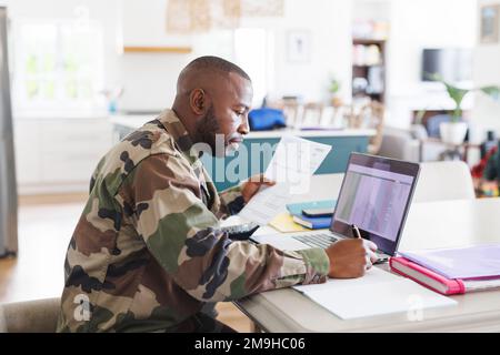 Happy african american man wearing military uniform sitting at table and working Stock Photo