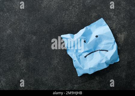 Blue crumpled sticky notes blank with drawing sad face on black background with copy space ready for your message. Blue Monday and mental health conce Stock Photo