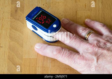 A woman using a pulse oximeter to measure the amount of oxygen in her blood. Stock Photo