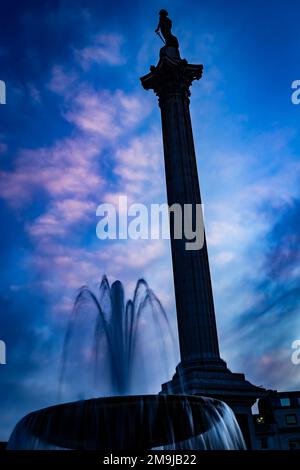 Trafalgar Square With Nelson's Column and dramatic fountain scene against a dark blue atmospheric sky.White and pink clouds and back light adds drama Stock Photo