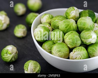 Close up of organic brussel sprouts in a white bowl on black stone background Stock Photo