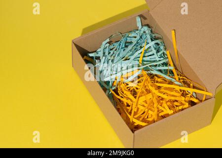 Gift wrap. Box with yellow and blue paper filling. Top view from above. Copy space. Cardboard carton flat box with paper filler on background. Brown paper box with shock safe. Wrapping Stock Photo