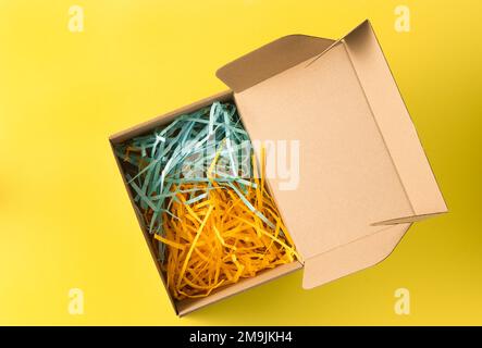 Gift wrap. Box with yellow and blue paper filling. Top view from above. Copy space. Cardboard carton flat box with paper filler on background. Brown paper box with shock safe. Wrapping Stock Photo