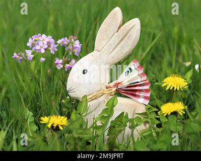 wooden easter bunny with euro banknote in green spring meadow between flowers, money gifts at easter concept image Stock Photo