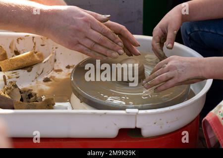 Making A Clay Pot On The Pottery Class. Potter working with student on potters wheel making ceramic pot from clay in pottery workshop on outdoor at No Stock Photo