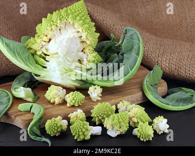 fresh romanesco broccoli, roman cauliflower in florets on wooden cutting board, preparing healthy cabbage vegetables Stock Photo