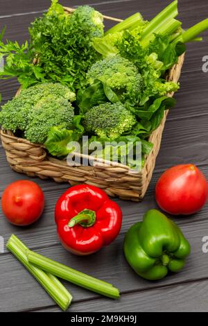 Tomatoes and peppers on the table. Lettuce, broccoli and celery stalks in a wicker basket. Top view. Dark wooden background. Stock Photo