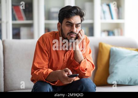 Bored middle eastern guy sitting at home, switching tv Stock Photo