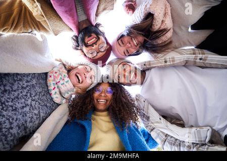 Multiracial group of happy friends doing a circle embracing, looking down to the camera cheerfully. Stock Photo