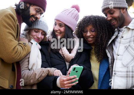 Group of multiethnic friends looking at mobile phone, laughing and sharing. Stock Photo