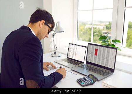 Accountant writing something while working with digital sheets on office computers Stock Photo