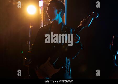 Rockstar woman with leather jacket holding electric guitar while performing heavy metal song, working at rock album in studio. Musician person playing punk music, adjusting electricinstrument Stock Photo