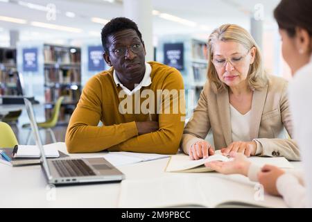 Female tutor helping students preparing for exam in library Stock Photo