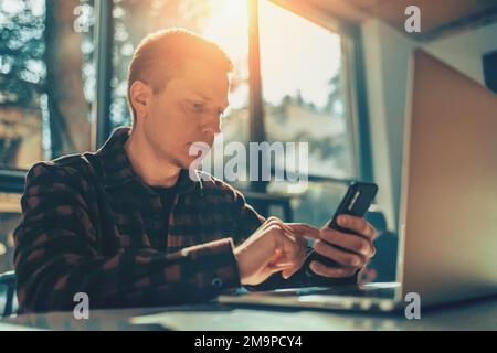 Cheerful freelancer using laptop sitting at table in cafe in sunny day. Stock Photo