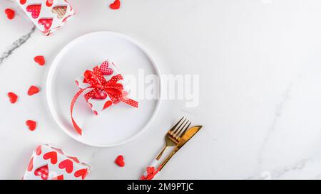 Valentines day dinner background with gifts, red hearts, fork and knife on white marble. Romantic holiday table setting Stock Photo