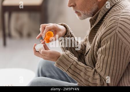 side view of cropped man suffering from parkinson disease holding pills container in trembling hands,stock image Stock Photo