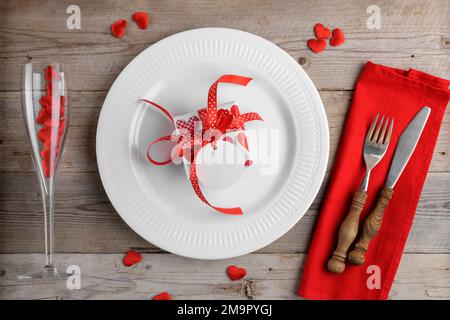 Valentines day dinner background with gift on white plate, cutlery and wine glass with red hearts on wooden background Stock Photo