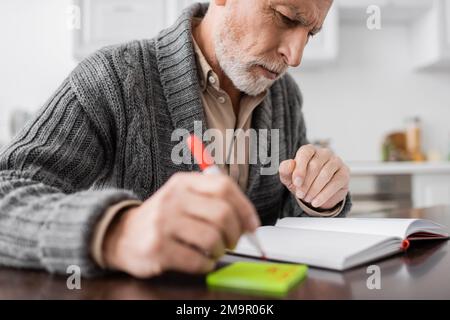 thoughtful man with alzheimer syndrome looking at blank notebook while holding blurred felt pen near sticky notes,stock image Stock Photo